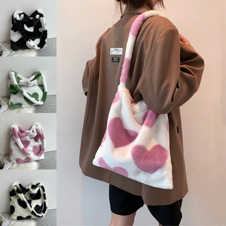 Woman wearing a brown jacket holding a white faux fur handbag with pink heart patterns, plus four similar patterned bags in black, green, purple, and black hearts