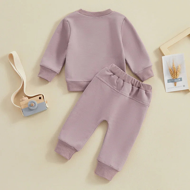 Lavender baby cotton sweater and pants set laid flat with wooden toy camera and framed wheat decoration