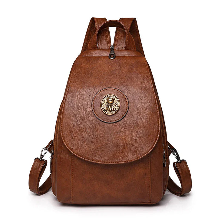 Brown leather backpack with gold lion emblem on front flap and adjustable straps
