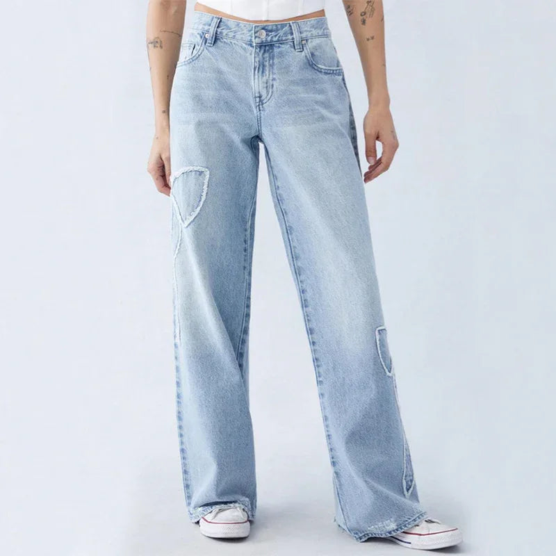 Light blue wide-leg jeans with patch details worn by model, paired with white sneakers