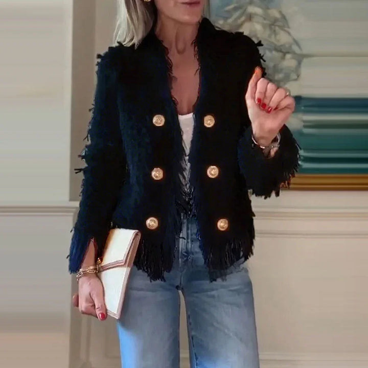 Woman wearing black textured blazer with gold buttons, blue jeans, white clutch, and red nail polish