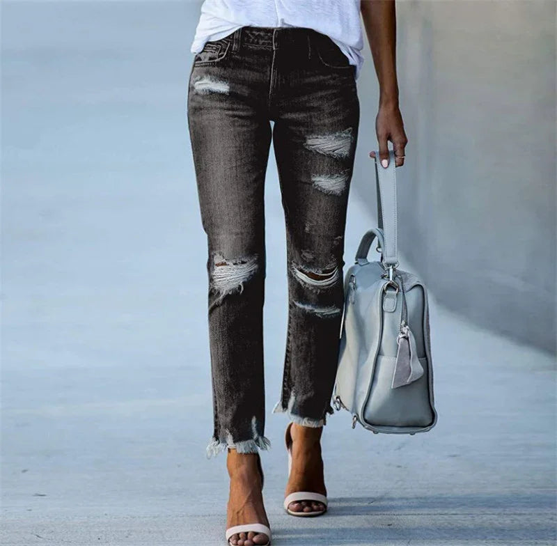 Woman wearing ripped black jeans and white heeled sandals carrying a gray handbag on street