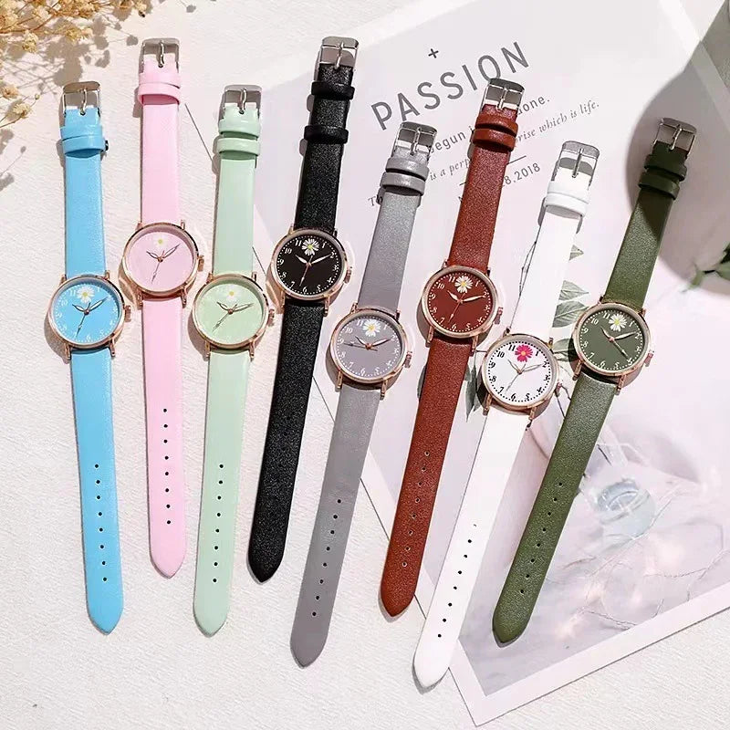 Eight wristwatches with colorful leather straps and floral watch faces arranged on a white surface with decorative paper