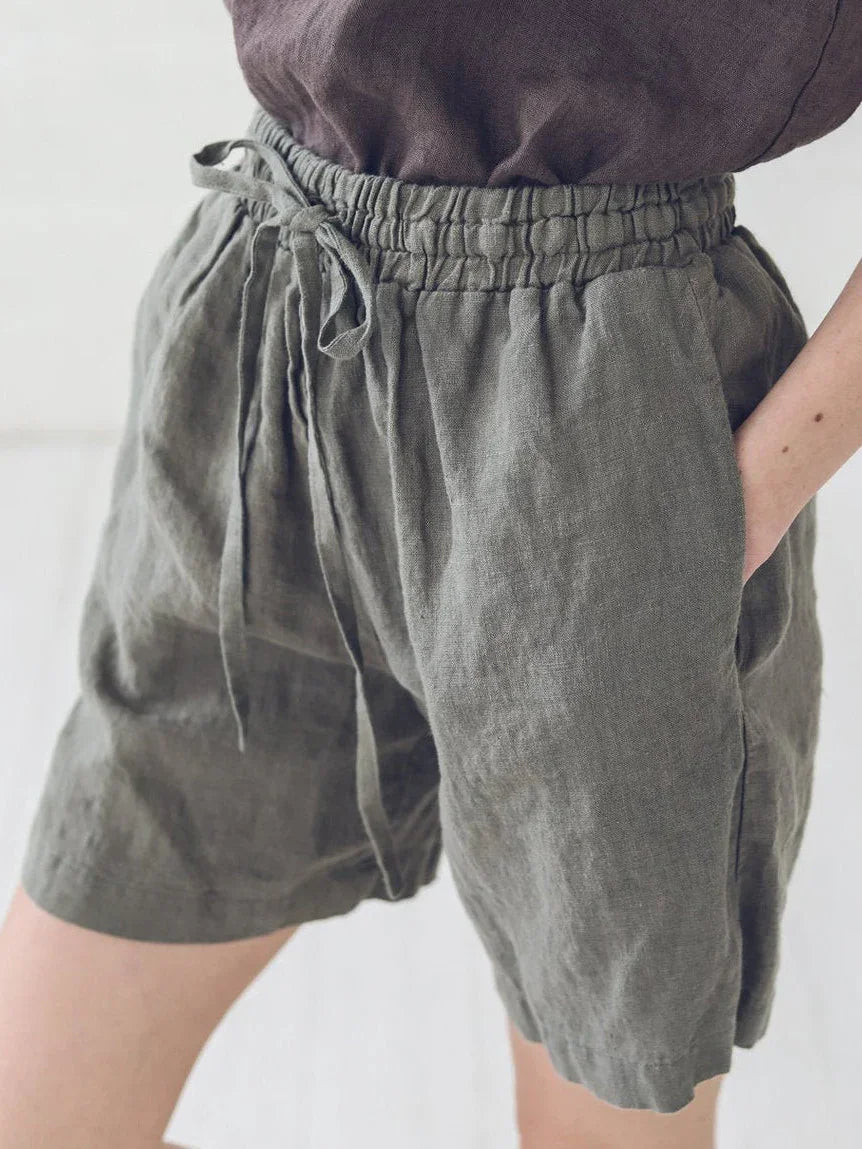 Close-up of person wearing olive green linen shorts with elastic drawstring waist and side pockets