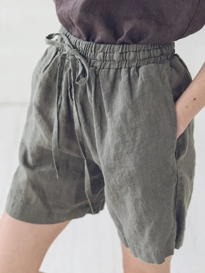 Close-up of person wearing olive green linen shorts with elastic waist and drawstring