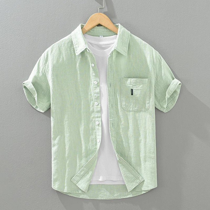 Light green short-sleeve linen shirt with chest pocket over white t-shirt on wooden hanger