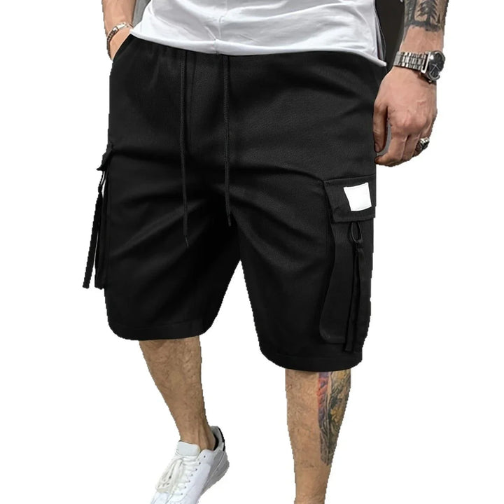 Men's black cargo shorts with side pockets, white sneakers, tattooed legs, casual outfit