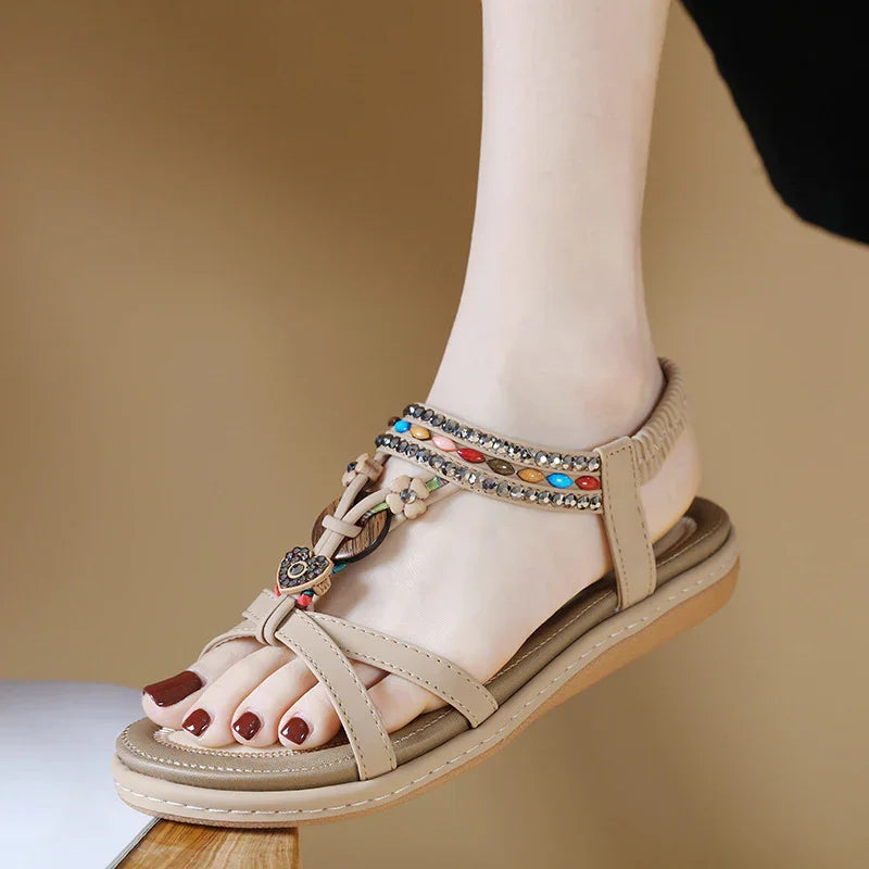 Beige flat sandals with colorful beads and gemstone accents worn on foot with dark red polished toenails