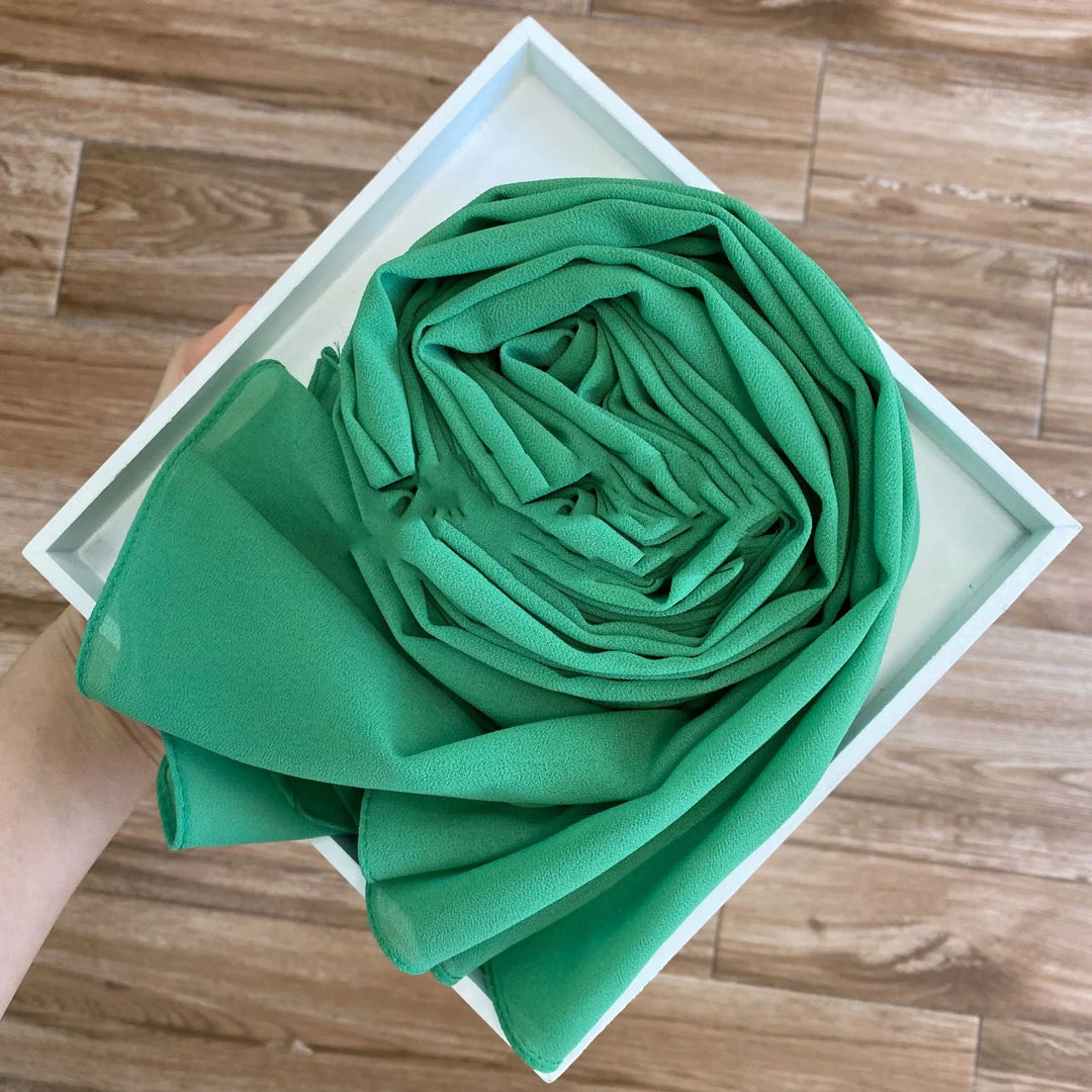 Hand holding white box with neatly rolled green chiffon fabric on wood floor background