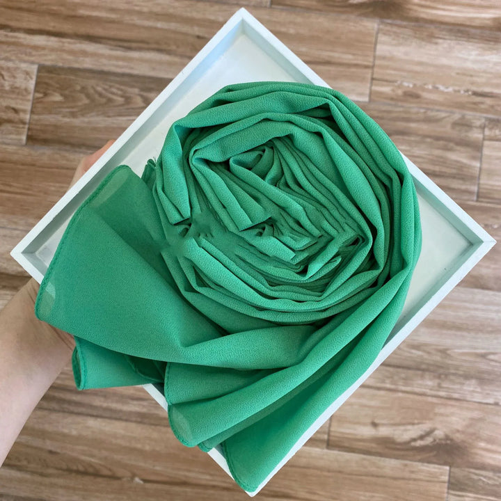Hand holding white box with neatly rolled green chiffon fabric on wood floor background