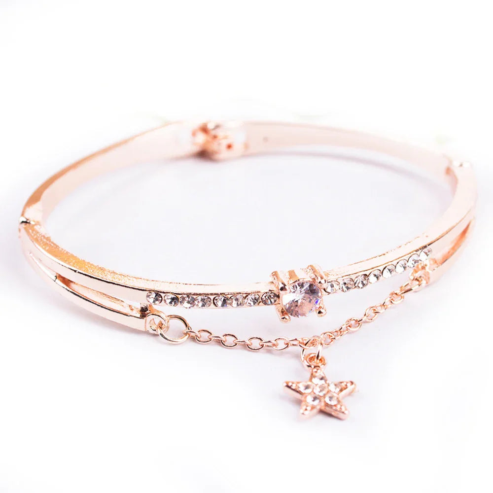 Rose gold bangle bracelet with clear crystals and dangling star charm on white background