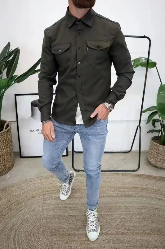 Man wearing dark green button-up shirt with pockets, light blue jeans, and patterned sneakers in modern room