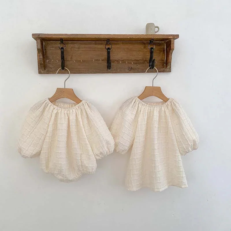 Two cream-colored textured puff-sleeve blouses hanging on wooden hangers on rustic wall hooks with a mug on top shelf