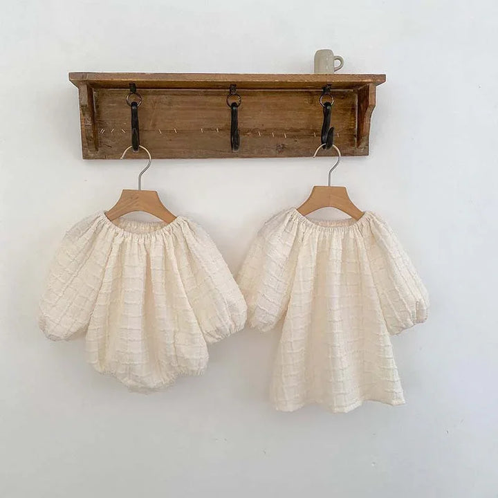 Two cream-colored textured puff-sleeve blouses hanging on wooden hangers on rustic wall hooks with a mug on top shelf