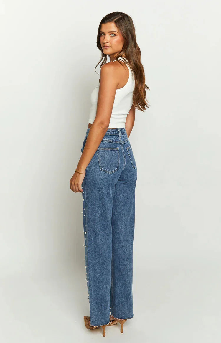 Woman in white tank top and high-waisted blue jeans with pearl side buttons, brown heels