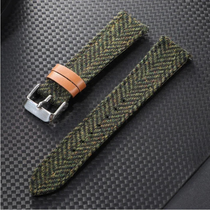 Green tweed fabric watch strap with brown leather loop and silver buckle on black textured surface