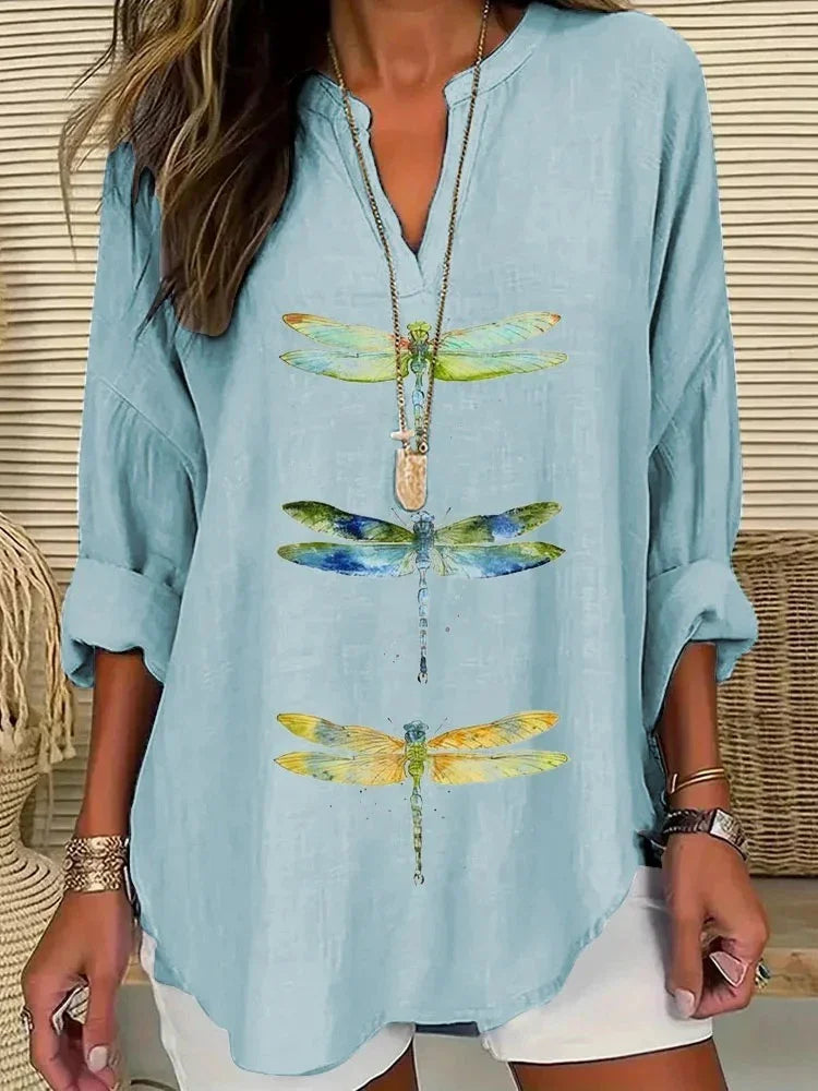 Woman wearing light blue long sleeve shirt with colorful dragonfly prints and white shorts