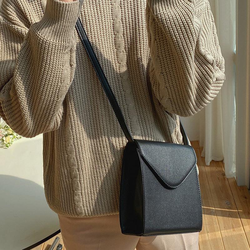 Person wearing beige cable knit sweater and pants with black leather crossbody bag in sunlit room