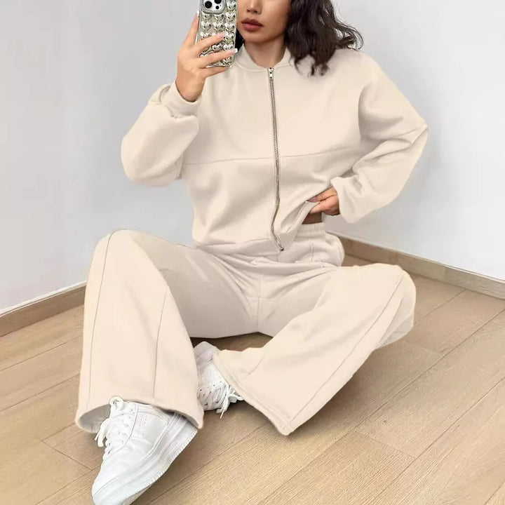 Woman wearing beige zip-up sweatshirt and matching wide-leg pants with white sneakers sitting on wooden floor