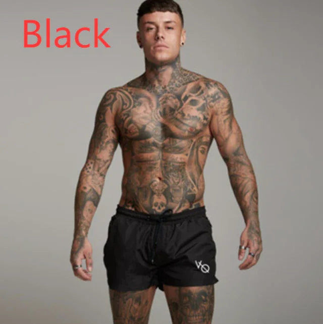 Tattooed muscular man wearing black shorts standing against gray background