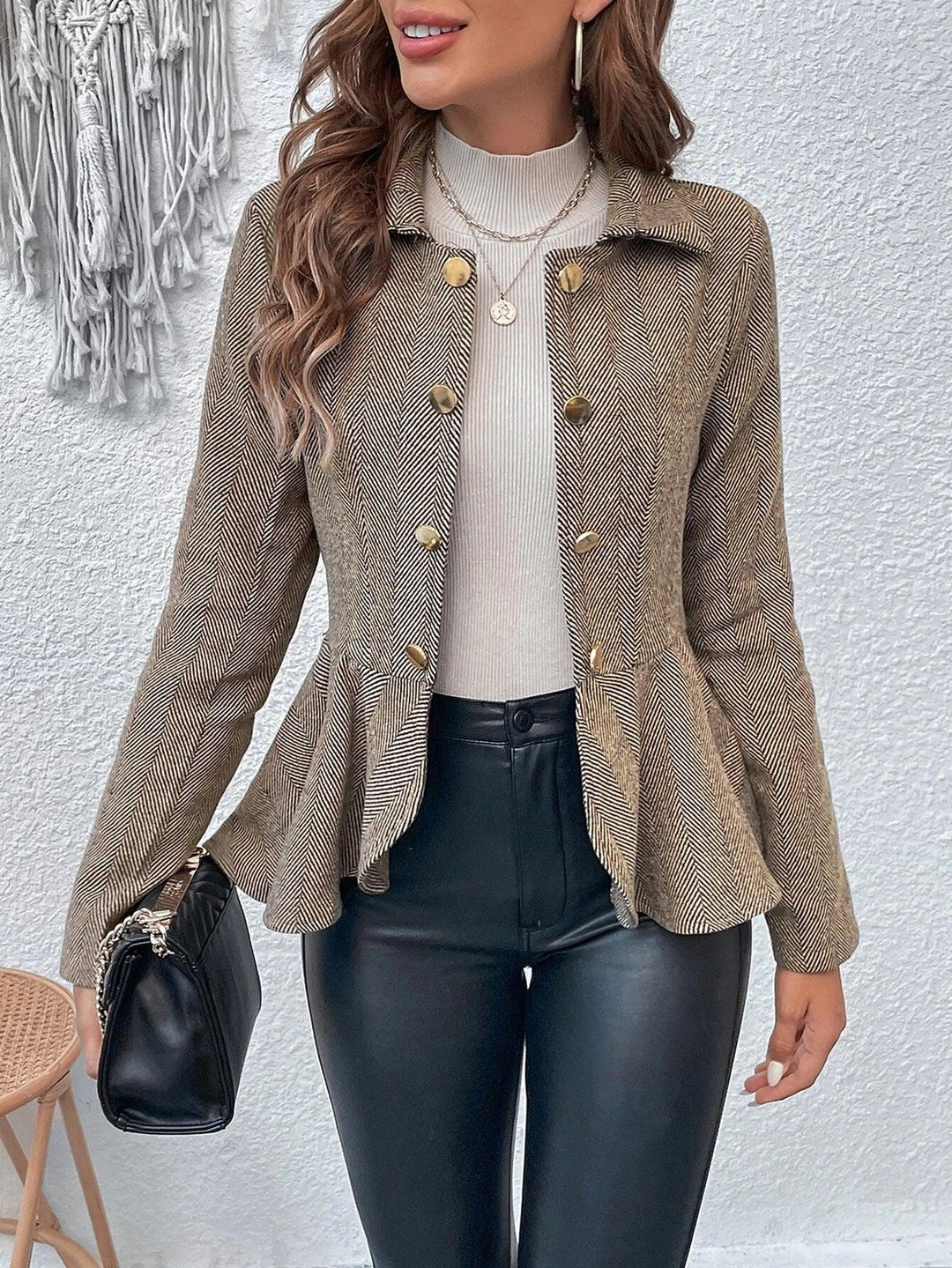 Woman wearing beige herringbone peplum blazer with gold buttons, cream ribbed top, black leather pants, holding black handbag