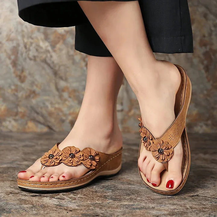 Close-up of feet wearing brown floral leather wedge sandals with red toenail polish on stone floor