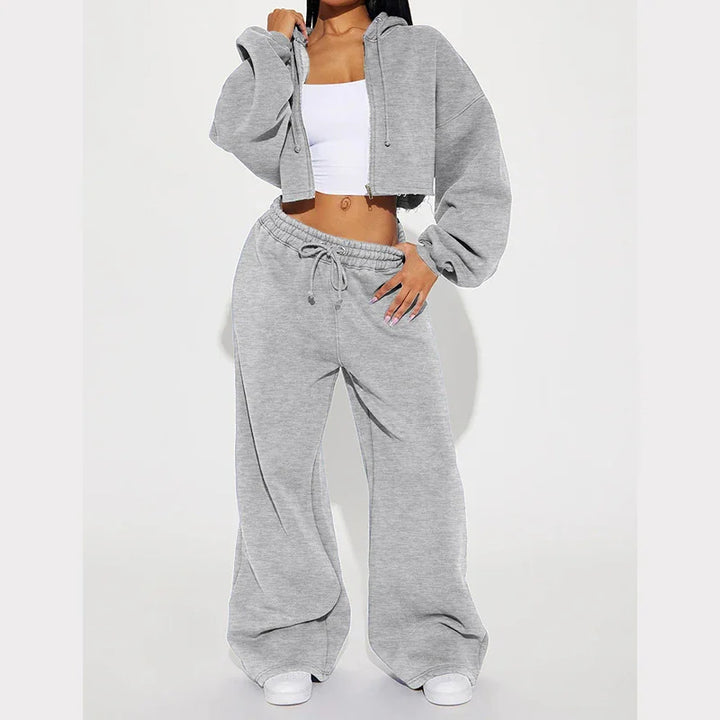 Woman wearing light gray cropped hoodie and wide-leg sweatpants with white crop top and sneakers