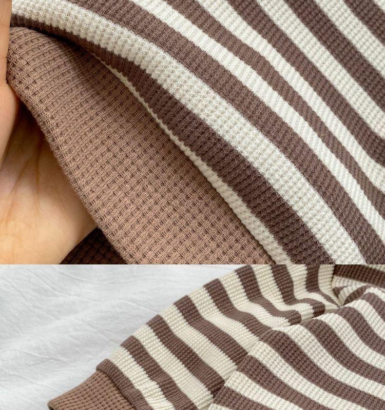 Close-up of brown and cream striped waffle knit fabric with hand holding the textile