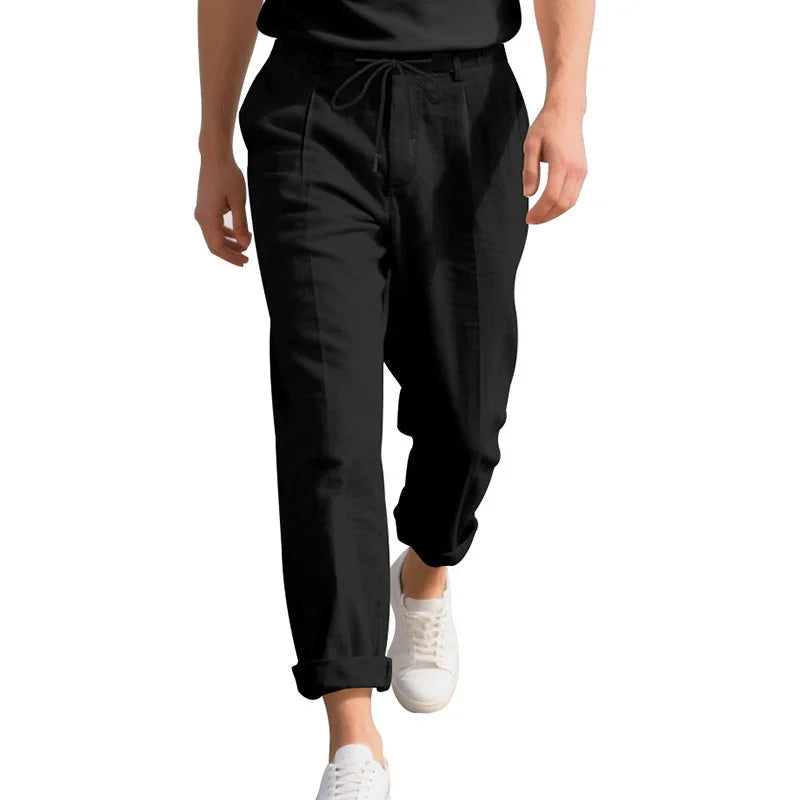 Man wearing black casual drawstring pants rolled at ankles with white sneakers on white background