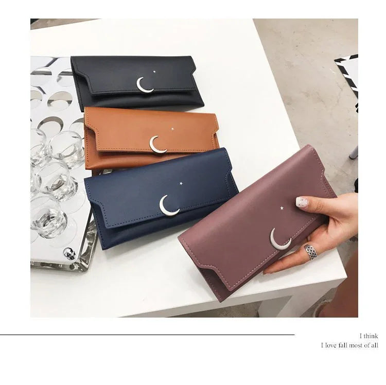 Four leather wallets in black, brown, navy, and mauve with crescent moon and star designs on a white table