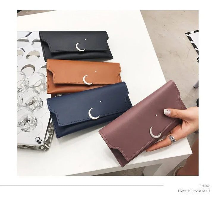 Four leather wallets in black, brown, navy, and mauve with crescent moon and star designs on a white table