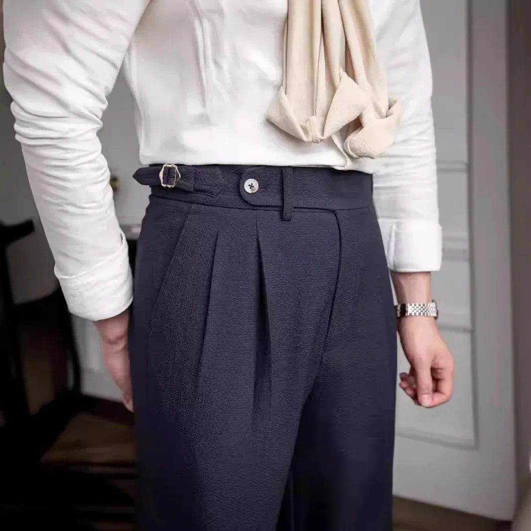 Man wearing navy pleated trousers with white shirt and beige scarf in indoor setting