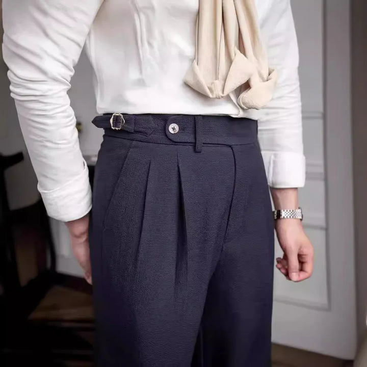 Man wearing navy pleated trousers with white shirt and beige scarf in indoor setting