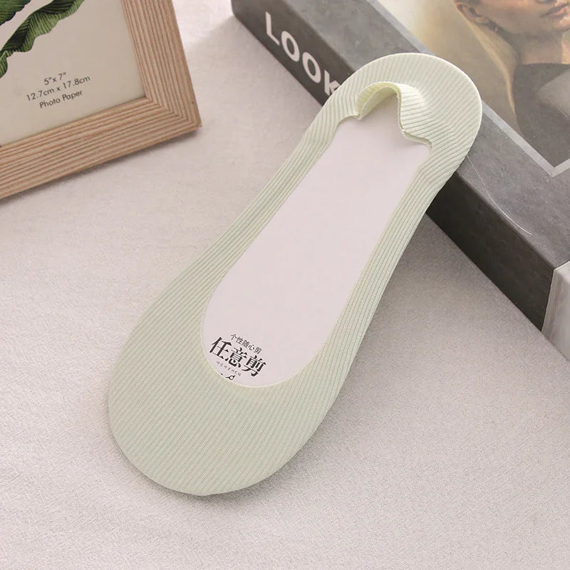 Light green ribbed no-show liner sock on beige fabric surface with framed photo and book