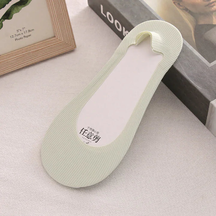 Light green ribbed no-show liner sock on beige fabric surface with framed photo and book