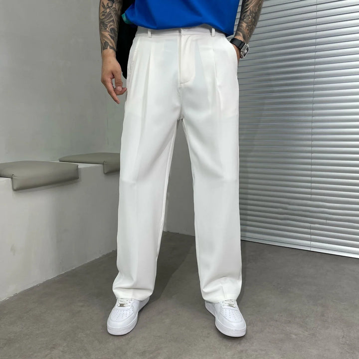 Man wearing white pleated trousers and white sneakers in a modern indoor setting