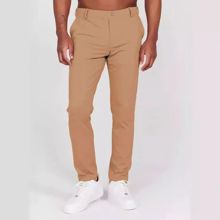 Man wearing slim-fit tan chinos and white sneakers on plain background
