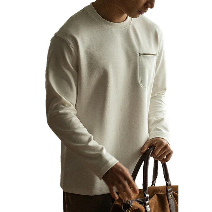 Man wearing white long-sleeve shirt with chest pocket holding brown leather duffle bag