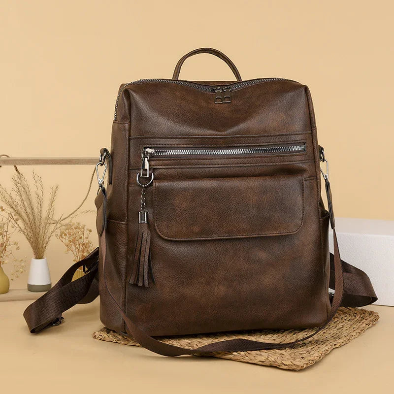 brown leather backpack with front zipper pocket and tassel on woven mat with beige background