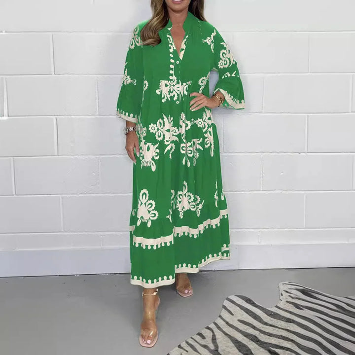 Woman wearing green and white floral embroidered long dress with sheer heels, against white brick wall