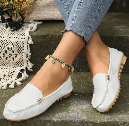 White casual loafers with tan soles worn with blue rolled-up jeans and seashell anklet on stone steps