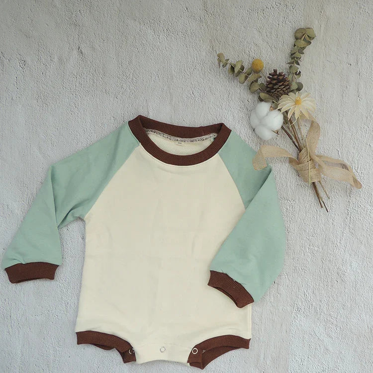 Baby long-sleeve onesie with green sleeves and brown trim, laid flat next to dried floral bouquet