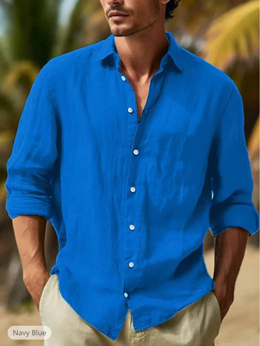 Man wearing navy blue linen shirt with rolled sleeves standing outdoors with blurred palm trees