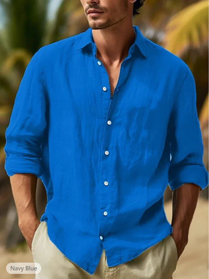Man wearing navy blue linen shirt with rolled sleeves standing outdoors with blurred palm trees