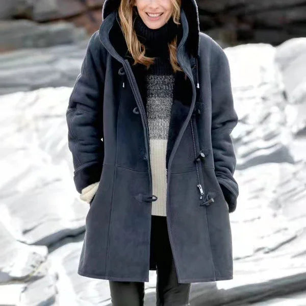 Woman wearing a dark hooded winter coat over a black and white sweater standing outdoors on rocky terrain