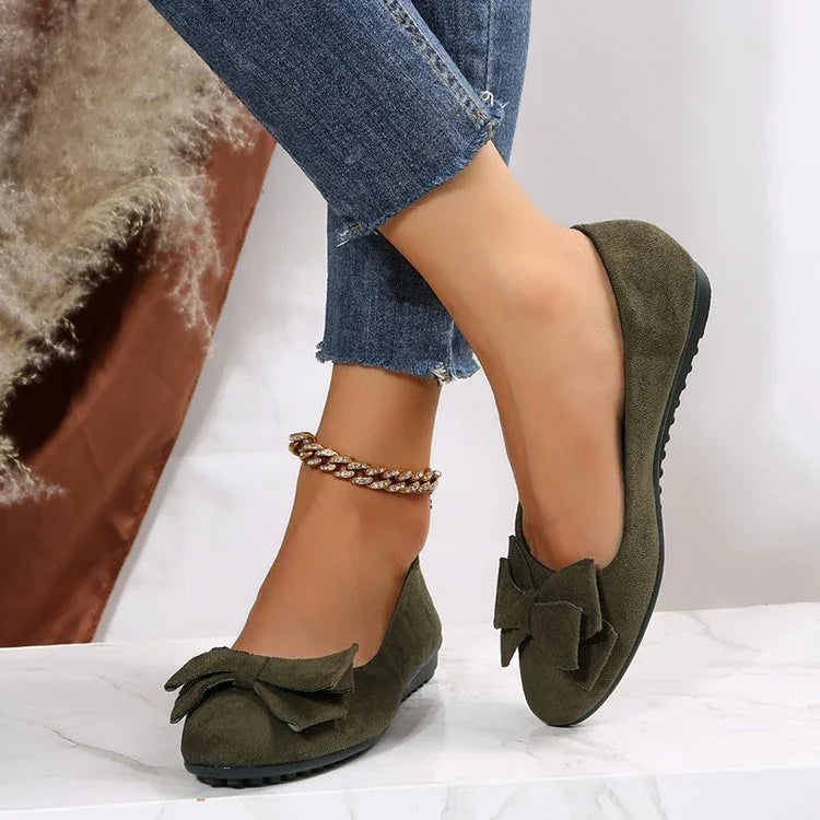 Woman wearing green suede ballerina flats with bow detail and ankle bracelet against white background