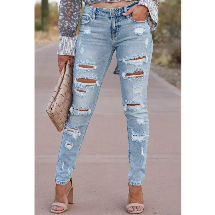 Woman wearing light blue distressed ripped skinny jeans and beige heels holding a tan woven clutch on outdoor path