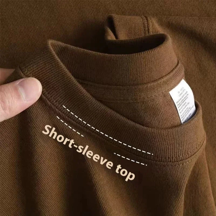 Brown short-sleeve top fabric close-up with hand holding neckline and clothing label visible