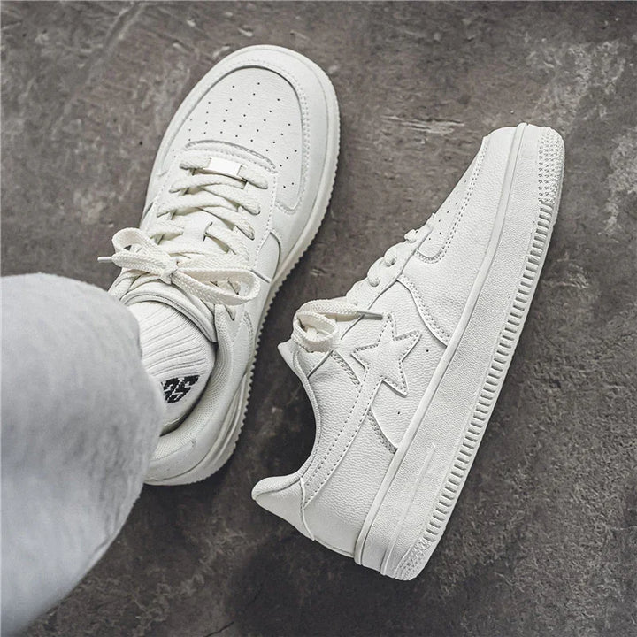 Pair of white leather sneakers with star design on concrete floor, casual streetwear shoes