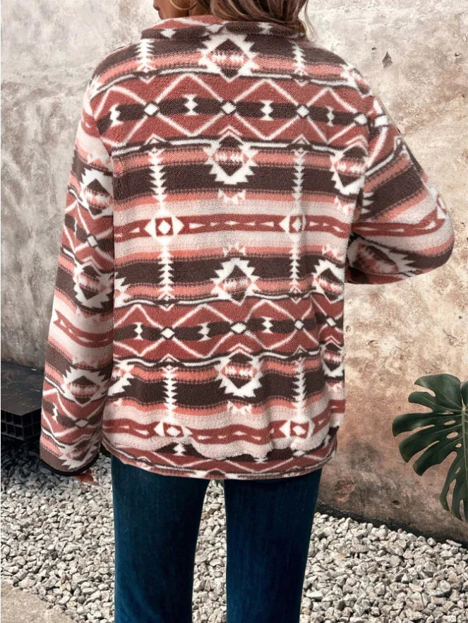 Woman wearing rust and white tribal patterned fleece jacket outdoors on gravel with green plant